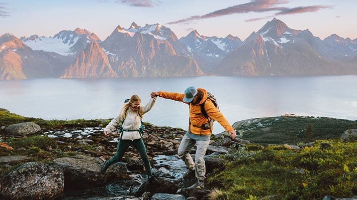 Symbolbild für finanzielle Freiheit: Ein fröhliches, junges Paar befindet sich auf einer Wanderung – im Hintergrund sind ein grosser See und eine Bergkette zu sehen.