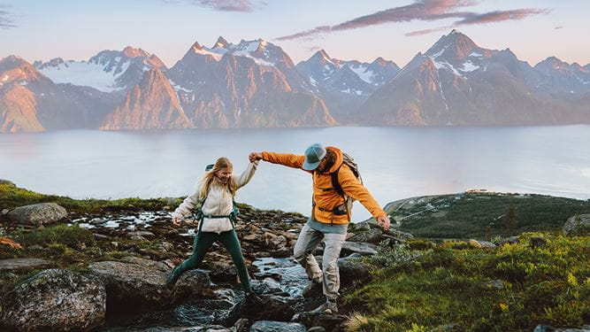 Symbolbild für finanzielle Freiheit: Ein fröhliches, junges Paar befindet sich auf einer Wanderung – im Hintergrund sind ein grosser See und eine Bergkette zu sehen.