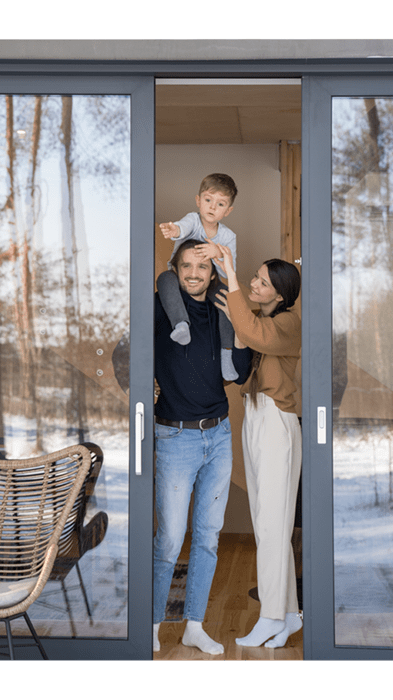Eine junge Familie blickt auf die verschneite Terrasse vom Wohnzimmer ihres Eigenheims aus.