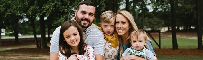 Ein Familie bestehend aus Vater, Mutter, Tochter, Sohn und Baby schaut lächelnd in die Kamera.