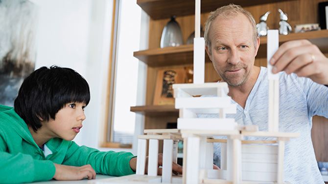 Ein Vater und sein Sohn bauen zusammen ein Haus aus Bauklötzen.