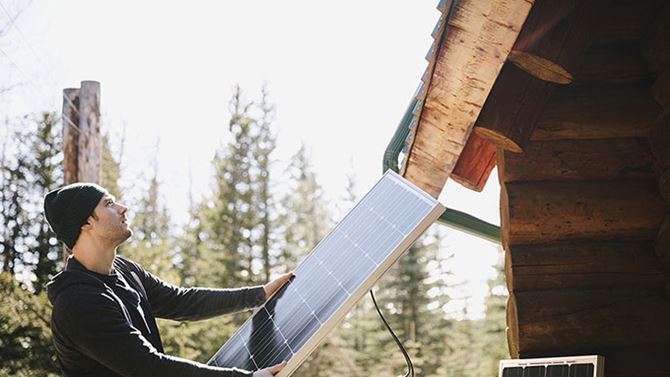 Ein Mann montiert ein Solarpanel auf dem Dach eines Chalets.