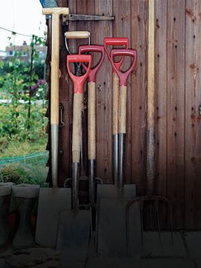 Diverse pale e una forca sono appoggiate alla parete di una casetta da giardino.